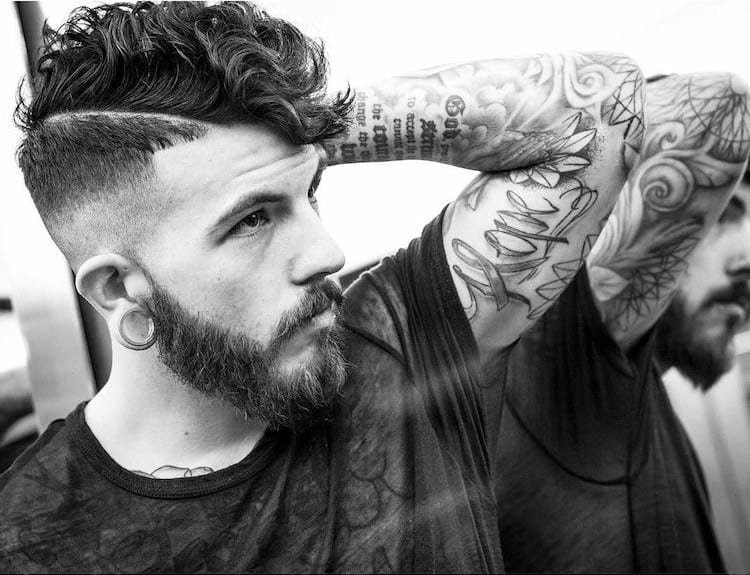 A man in black printed t-shirt and tattoos on his hands showing his High Fade Curly - Latest Hair Cut for Men and Boys