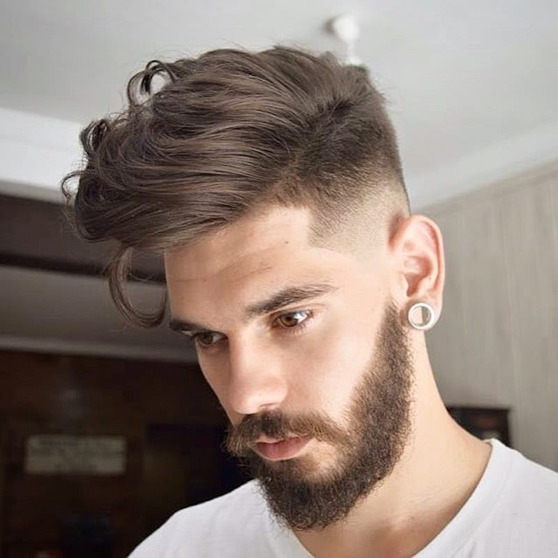 A man in white V-neck t-shirt and earring showing the side view of his Long Wavy and High Fade - Hairstyles for men 2022