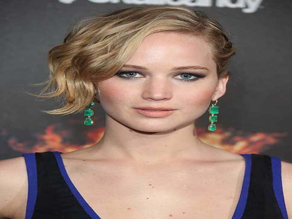 Jennifer Lawrence in blue and black cut sleeves dress and green drop earrings posing for camera - celebrity hairstyle