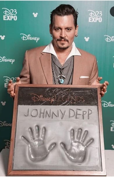 Johnny Depp in in brown suit showing his hand painting -  Johnny Depp hairstyle