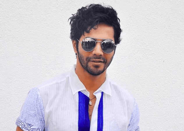 Varun Dhawan in blue and white shirt with goggles posing for camera and showing his Ruffled messy hairstyles - Varun Dhawan Hairstyles