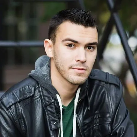 Man in black jacket with green t-shirt and Back Haul hairstyle - haircuts for men with beards