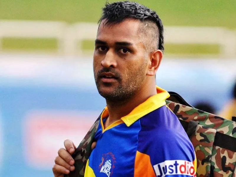 MS Dhoni in blue and yellow t-shirt with a bag showing his hairstyle - MS Dhoni hairstyles