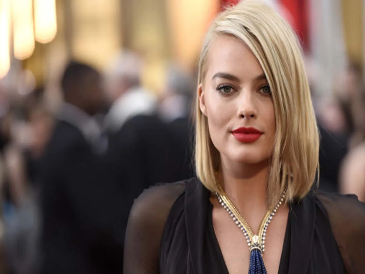 Margot Robbie in black dress with blue and golden necklace posing for camera - celebrity hairstyle