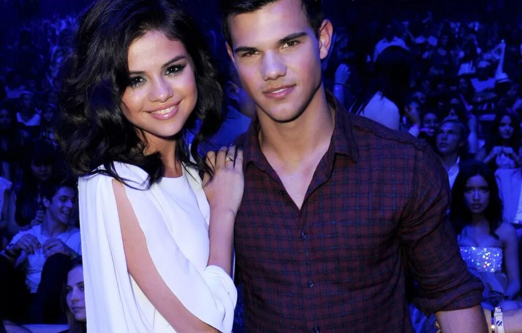 Selena Gomez in white dress and Taylor Lautner in check shirt posing for camera Selena Gomez in white dress and Taylor Lautner in check shirt posing for camera - selena gomez