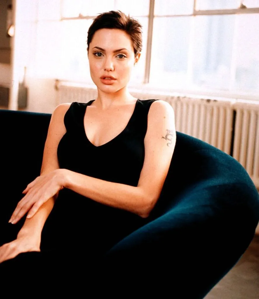Angelina Jolie sitting on a couch wearing black tank top - short hair hollywood celebrities