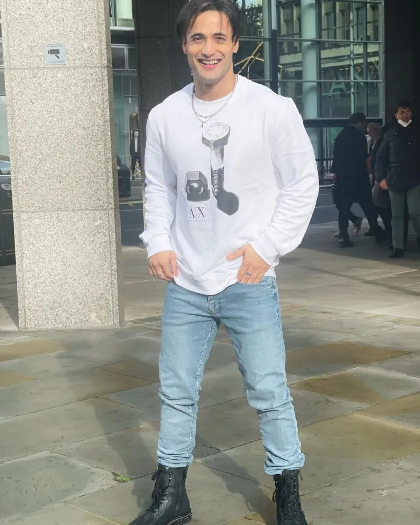 Smiling Asim Riaz in white full sleeves t-shirt with light blue jeans and boots posing for camera Smiling Asim Riaz in white full sleeves t-shirt with light blue jeans and boots posing for camera - most handsome tv actors indian
