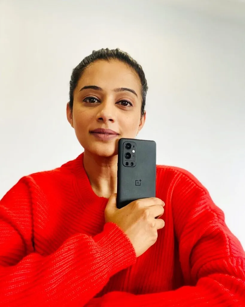 Priyamani in red sweater holding a phone ad showing her no makeup look Priyamani in red sweater holding a phone ad showing her no makeup look - south actress without makeup