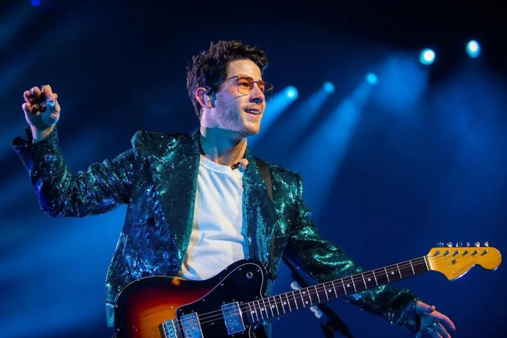 Nick Jonas in blue shimmery jacket with white t-shirt and goggles holding an guitar Nick Jonas in blue shimmery jacket with white t-shirt and goggles holding an guitar - indian celebrities with diabetes type 1