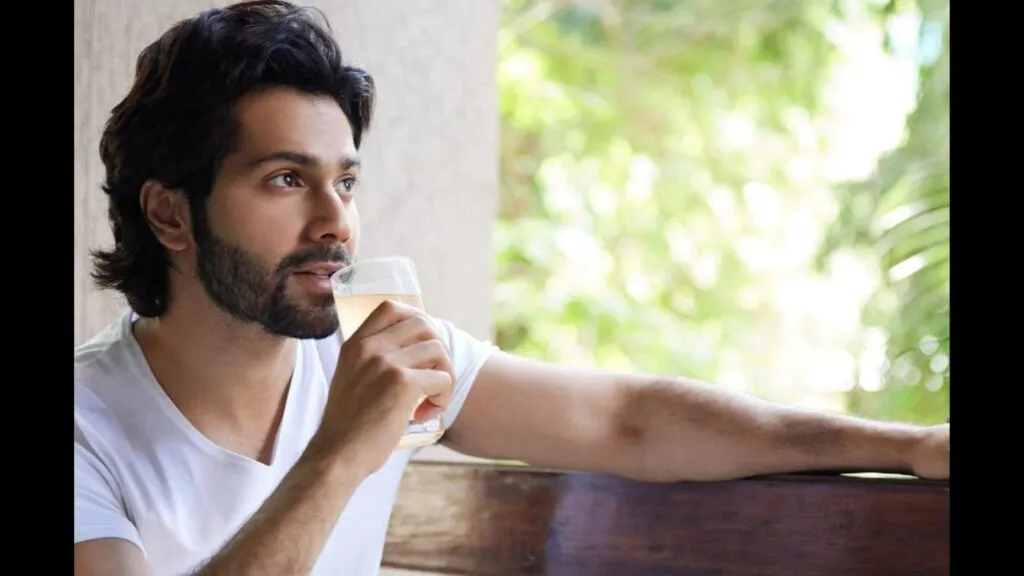 Varun Dhawan in white t-shirt sitting and drinking water Varun Dhawan in white t-shirt sitting and drinking water - Varun Dhawan hair care routine